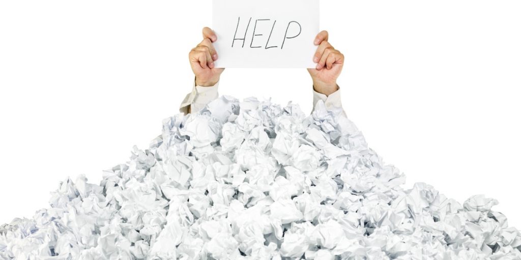 Person holding Help sign buried in pile of paper