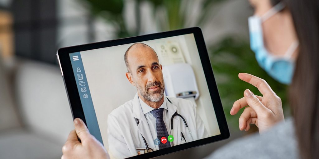 Woman wearing face mask using tablet to speak to doctor via telemedicine